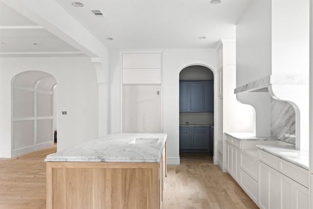 6207 Marquita Ave, Dallas, TX 75214 - kitchen with arched walkways, light wood-type flooring, white cabinets, light stone countertops, and a kitchen island