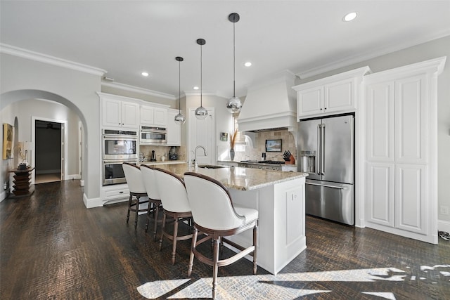 415 Fountainview Dr, Irving, TX 75039 - kitchen featuring appliances with stainless steel finishes, premium range hood, arched walkways, tasteful backsplash, and a breakfast bar