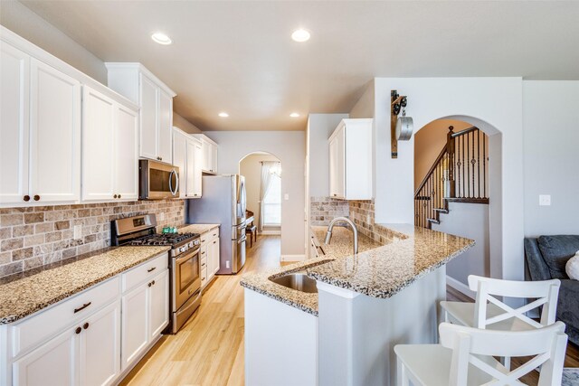3501 Brazos St, Melissa, TX 75454 - kitchen featuring appliances with stainless steel finishes, a sink, arched walkways, light wood-type flooring, and a kitchen breakfast bar