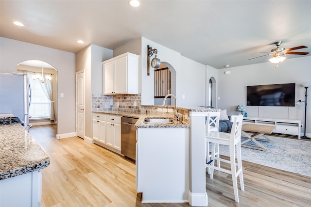 3501 Brazos St, Melissa, TX 75454 - kitchen featuring arched walkways, stainless steel appliances, light stone counters, a peninsula, and light wood finished floors