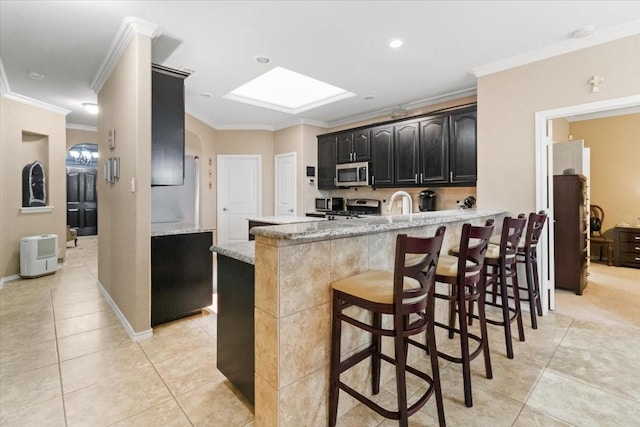 1407 Deer Hollow Dr, Arlington, TX 76002 - kitchen with stainless steel appliances, light tile patterned flooring, ornamental molding, dark cabinetry, and a kitchen breakfast bar