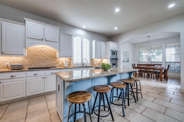 590 Willow Ridge Cir, Prosper, TX 75078 - kitchen with stainless steel appliances, a sink, arched walkways, a kitchen island, and backsplash
