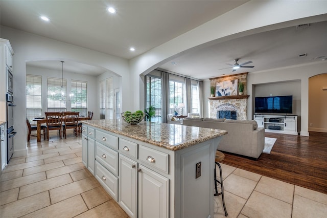 590 Willow Ridge Cir, Prosper, TX 75078 - kitchen with a ceiling fan, a kitchen island, light tile patterned floors, white cabinetry, and a fireplace
