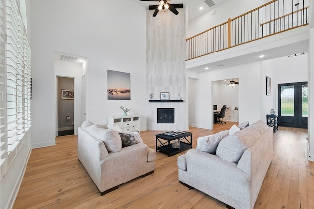 1301 Limestone Ridge Rd, Mansfield, TX 76063 - living room with a towering ceiling, a ceiling fan, a tiled fireplace, french doors, and light wood-type flooring