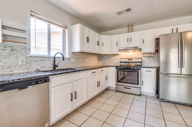 1709 Meadow Vly, Irving, TX 75060 - kitchen featuring appliances with stainless steel finishes, under cabinet range hood, a sink, dark stone counters, and white cabinetry