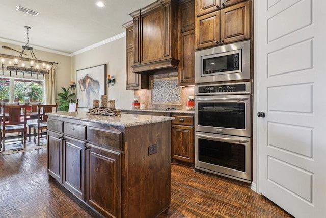 114 Piper Pkwy, Waxahachie, TX 75165 - kitchen with a chandelier, appliances with stainless steel finishes, crown molding, light stone counters, and a kitchen island