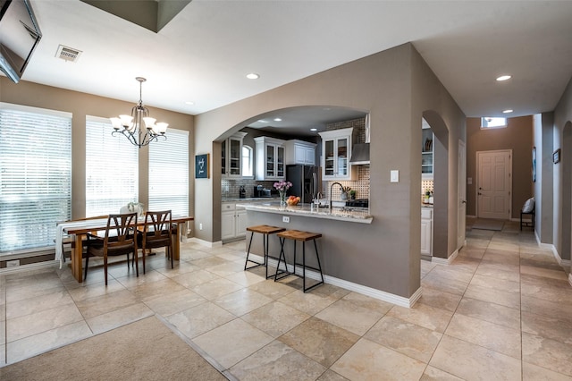 6312 Valley View Dr, Mckinney, TX 75071 - kitchen with black refrigerator with ice dispenser, decorative backsplash, a kitchen breakfast bar, a chandelier, and arched walkways