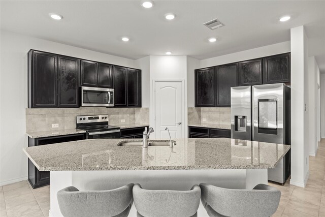 1028 W Dr, Aubrey, TX 76227 - kitchen with stainless steel appliances, dark cabinetry, a sink, light stone counters, and recessed lighting