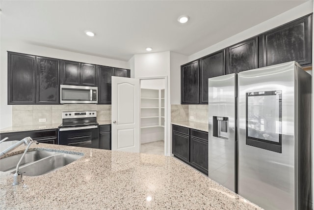 1028 W Dr, Aubrey, TX 76227 - kitchen with stainless steel appliances, dark cabinets, a sink, backsplash, and light stone counters