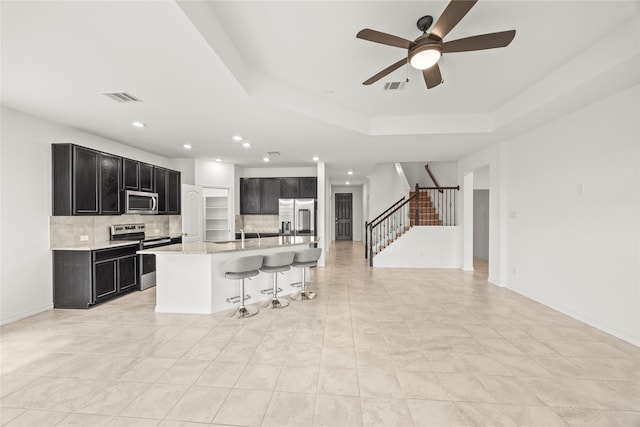 1028 W Dr, Aubrey, TX 76227 - kitchen with stainless steel appliances, dark cabinetry, decorative backsplash, a kitchen bar, and a ceiling fan