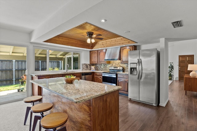 4208 Crestover Dr, Mesquite, TX 75150 - kitchen featuring appliances with stainless steel finishes, wall chimney exhaust hood, a tray ceiling, dark wood finished floors, and recessed lighting