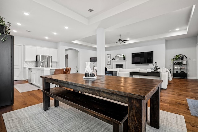 2705 Cumberland, The Colony, TX 75056 - dining space featuring a tray ceiling, ceiling fan, recessed lighting, arched walkways, and a glass covered fireplace