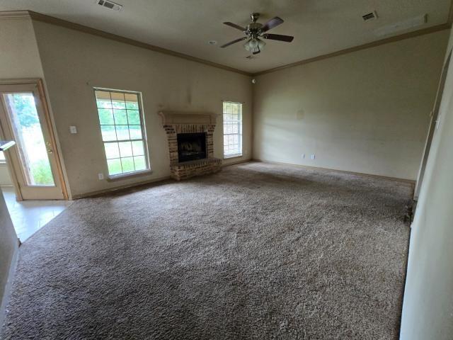 unfurnished living room featuring ceiling fan, crown molding, a brick fireplace, carpet flooring, and baseboards