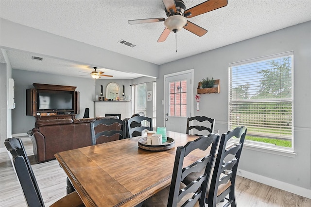 2748 Yoakum St, Fort Worth, TX 76108 - dining space featuring ceiling fan, light wood-style flooring, a brick fireplace, healthy amount of natural light, and a textured ceiling