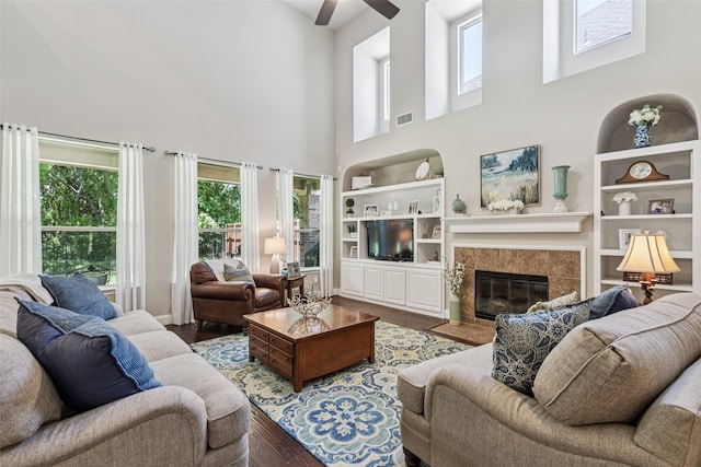 11310 Seguin Dr, Frisco, TX 75035 - living area with wood finished floors, a high ceiling, ceiling fan, a tile fireplace, and built in features