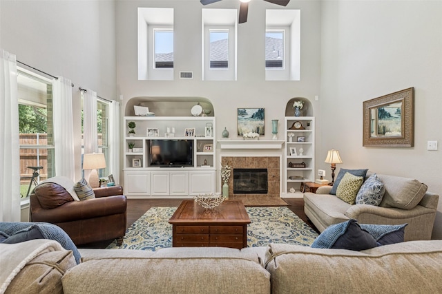11310 Seguin Dr, Frisco, TX 75035 - living room featuring a towering ceiling, wood finished floors, ceiling fan, built in shelves, and a tiled fireplace
