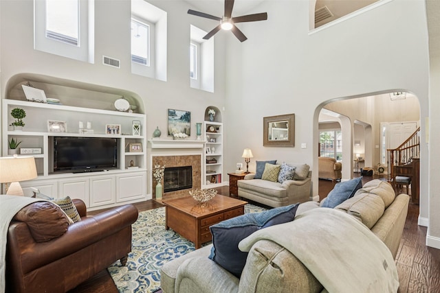 11310 Seguin Dr, Frisco, TX 75035 - living room featuring arched walkways, a ceiling fan, wood finished floors, a towering ceiling, and a tiled fireplace