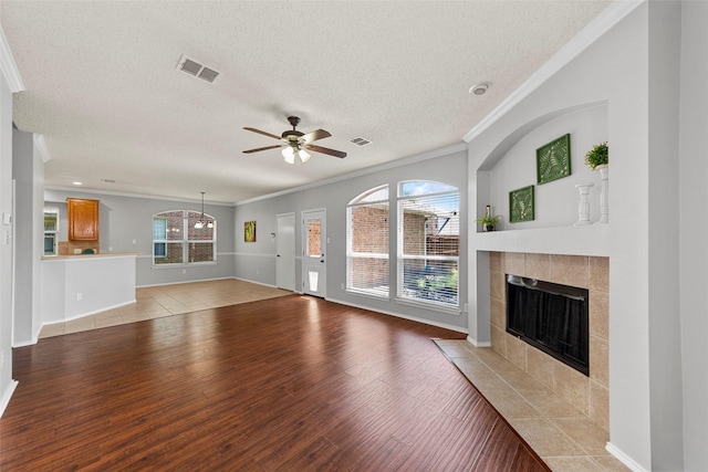 1106 Brook Ridge Ave, Allen, TX 75002 - unfurnished living room with crown molding, light wood-type flooring, a tile fireplace, a textured ceiling, and plenty of natural light