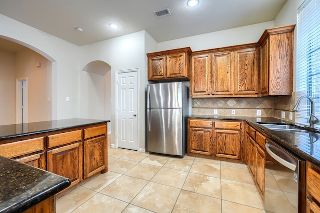 2128 Chambers Dr, Allen, TX 75013 - kitchen with stainless steel appliances, a sink, brown cabinets, backsplash, and arched walkways