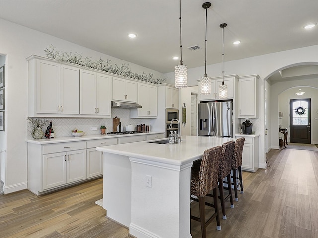 2624 Bellevue, The Colony, TX 75056 - kitchen featuring appliances with stainless steel finishes, a sink, under cabinet range hood, backsplash, and light wood finished floors