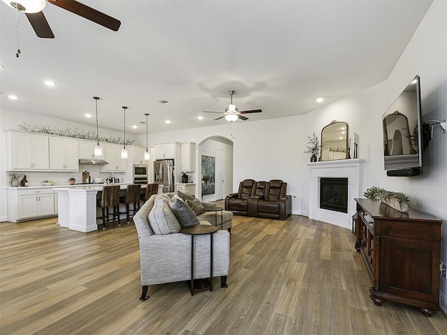 2624 Bellevue, The Colony, TX 75056 - living room featuring a ceiling fan, light wood finished floors, arched walkways, a glass covered fireplace, and recessed lighting