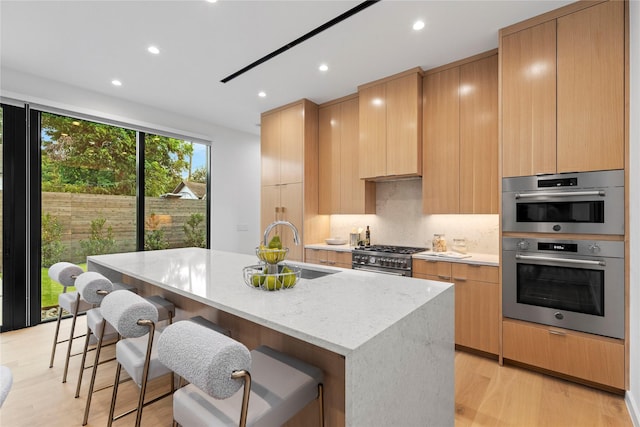 5029 Pershing St, Dallas, TX 75206 - kitchen with a sink, appliances with stainless steel finishes, a center island with sink, light stone countertops, and light wood-type flooring