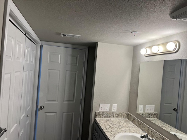 6108 Abrams Rd Unit 225, Dallas, TX 75231 - bathroom with vanity, a textured ceiling, and a wall mounted air conditioner