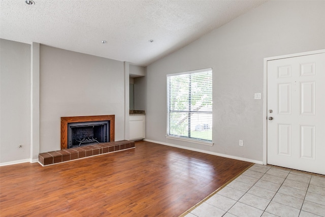 6646 E Lovers Ln Unit 602, Dallas, TX 75214 - unfurnished living room featuring lofted ceiling, wood finished floors, a fireplace, a textured ceiling, and baseboards