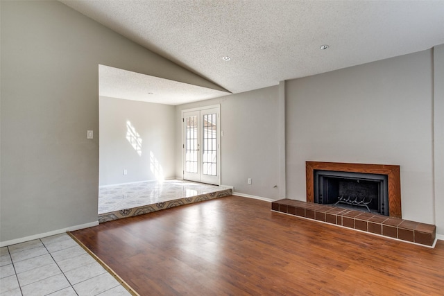 6646 E Lovers Ln Unit 602, Dallas, TX 75214 - unfurnished living room featuring vaulted ceiling, tile patterned floors, a tile fireplace, a textured ceiling, and baseboards
