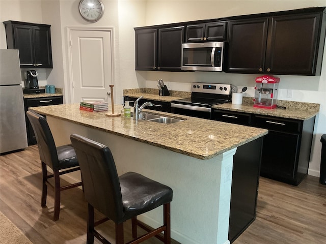 304 Gypsum Ln, Glenn Heights, TX 75154 - kitchen featuring stainless steel appliances, a sink, light wood finished floors, a kitchen bar, and dark cabinetry
