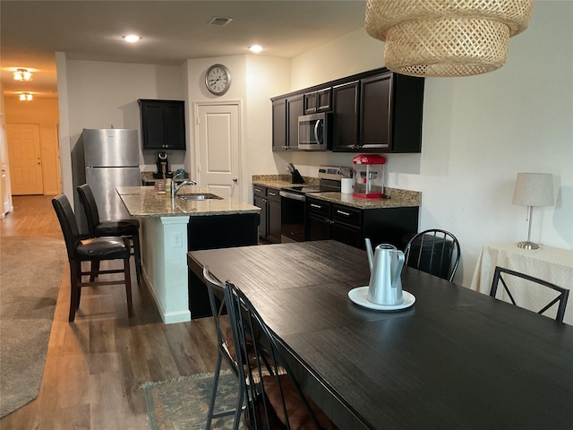 304 Gypsum Ln, Glenn Heights, TX 75154 - kitchen featuring stainless steel appliances, a sink, an island with sink, wood finished floors, and light stone countertops