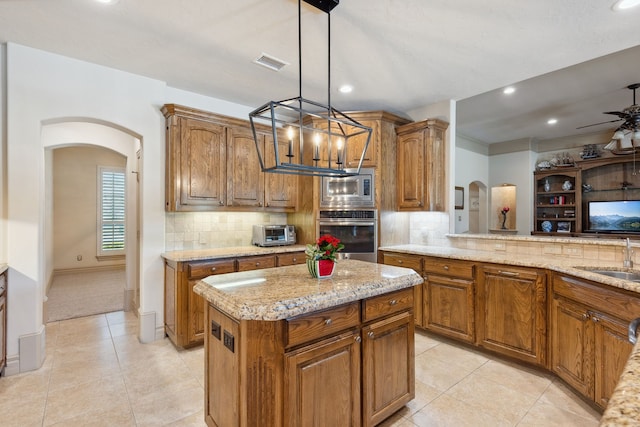 499 Savannah Hill Ln, Rockwall, TX 75032 - kitchen featuring appliances with stainless steel finishes, arched walkways, a sink, brown cabinets, and tasteful backsplash