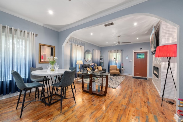 2832 Forest Ave, Fort Worth, TX 76112 - dining room with arched walkways, a tiled fireplace, light wood-type flooring, crown molding, and ceiling fan
