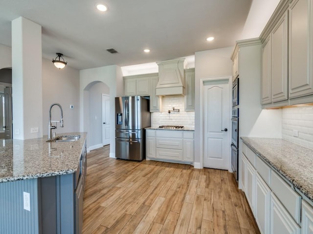 1517 Port Millstone Trl, Wylie, TX 75098 - kitchen with a sink, stainless steel appliances, arched walkways, premium range hood, and light wood-type flooring