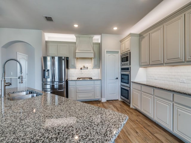 1517 Port Millstone Trl, Wylie, TX 75098 - kitchen with stainless steel appliances, a sink, custom range hood, light wood finished floors, and light stone counters