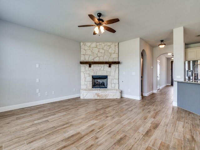 1517 Port Millstone Trl, Wylie, TX 75098 - unfurnished living room with a ceiling fan, arched walkways, light wood finished floors, a fireplace, and baseboards