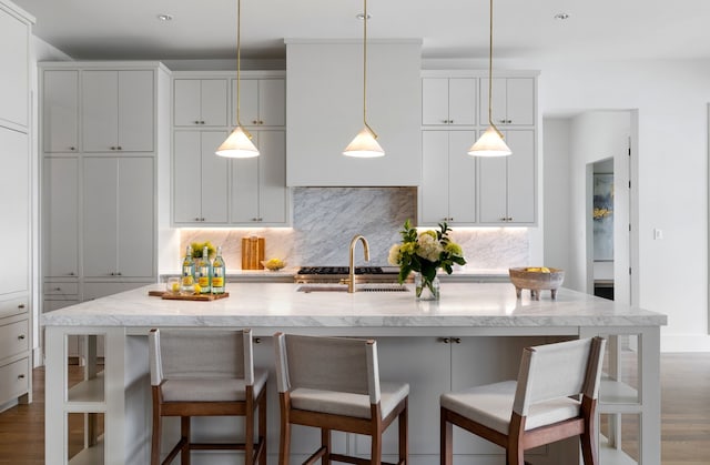 4207 Valley Ridge Rd, Dallas, TX 75220 - kitchen with backsplash, decorative light fixtures, an island with sink, light stone counters, and dark wood-style flooring