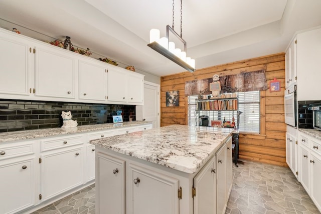 14213 Clark Dr, Streetman, TX 75859 - kitchen with decorative backsplash, wood walls, a kitchen island, white cabinetry, and light stone finish floors