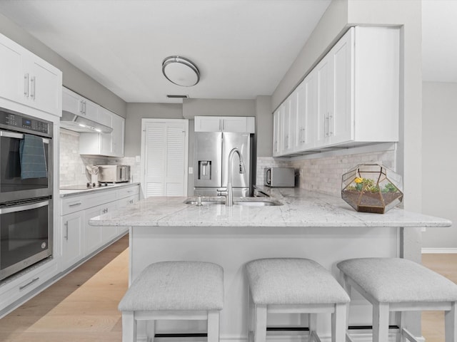 1507 Summertree Ct, Richardson, TX 75082 - kitchen featuring appliances with stainless steel finishes, a sink, a peninsula, and white cabinetry