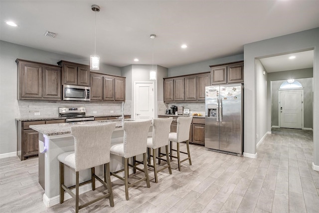 817 Nicole Way, Fort Worth, TX 76028 - kitchen with appliances with stainless steel finishes, light wood finished floors, a center island with sink, baseboards, and a breakfast bar area