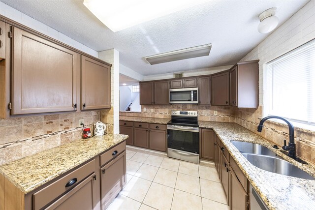 6900 Tudor Dr, Plano, TX 75023 - kitchen featuring stainless steel appliances, a sink, tasteful backsplash, light stone counters, and a textured ceiling