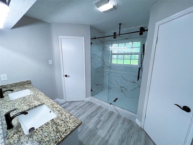2946 Ridgewood Dr, Grapevine, TX 76051 - bathroom featuring a marble finish shower, wood finished floors, double vanity, a textured ceiling, and baseboards
