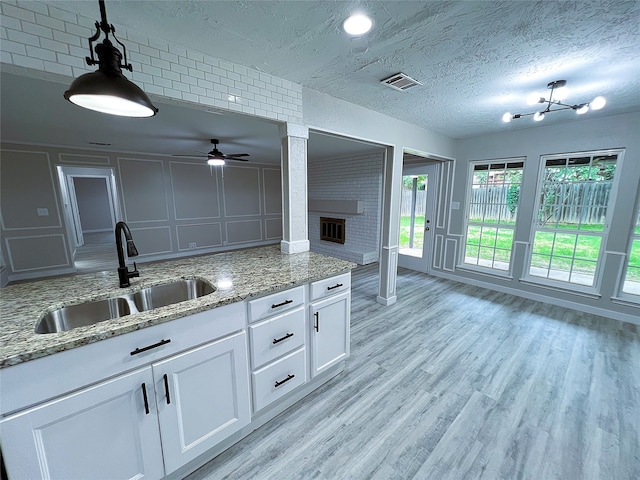 2946 Ridgewood Dr, Grapevine, TX 76051 - kitchen with a sink, a ceiling fan, a fireplace, light wood-style flooring, and a textured ceiling