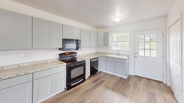 5604 5th St, Rochelle, TX 76872 - kitchen featuring black appliances, light wood-type flooring, gray cabinetry, a sink, and light stone countertops