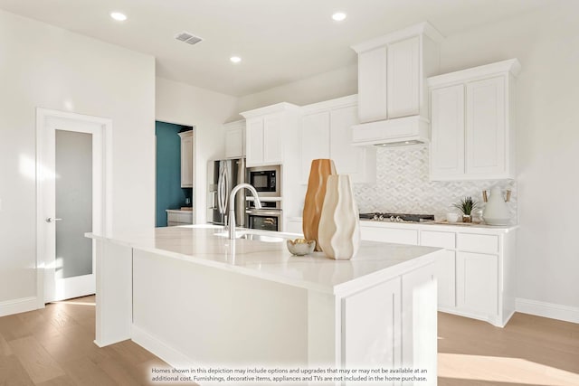 4622 Bel Air Dr, Midlothian, TX 76065 - kitchen featuring a sink, stainless steel appliances, light wood-type flooring, tasteful backsplash, and a kitchen island with sink
