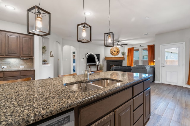 15712 Oak Pointe Dr, Fort Worth, TX 76177 - kitchen with a ceiling fan, a sink, arched walkways, a warm lit fireplace, and dark stone counters