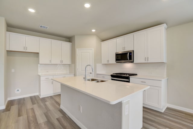 944 Linden Ct, Lavon, TX 75166 - kitchen with stainless steel microwave, gas stove, a sink, a center island with sink, and light wood-type flooring