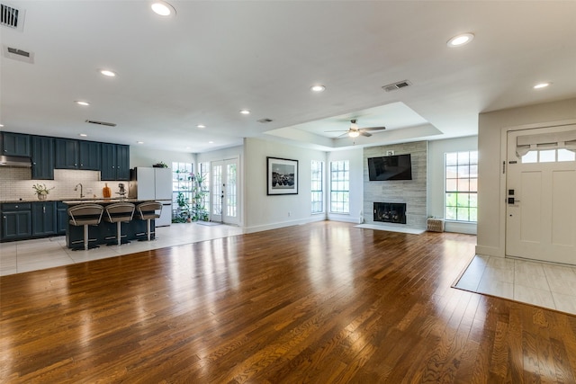 14815 Surveyor Blvd, Addison, TX 75001 - unfurnished living room with light wood-style floors, ceiling fan, a tray ceiling, a fireplace, and recessed lighting