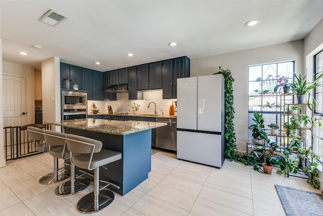 14815 Surveyor Blvd, Addison, TX 75001 - kitchen featuring appliances with stainless steel finishes, a breakfast bar, dark stone countertops, under cabinet range hood, and decorative backsplash