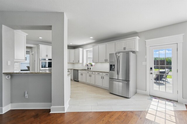 3752 Menard Dr, Carrollton, TX 75010 - kitchen featuring appliances with stainless steel finishes, a sink, light wood-style floors, baseboards, and white cabinets